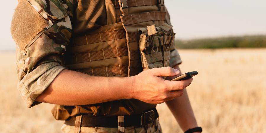 Military Army member holding a cell phone in a field