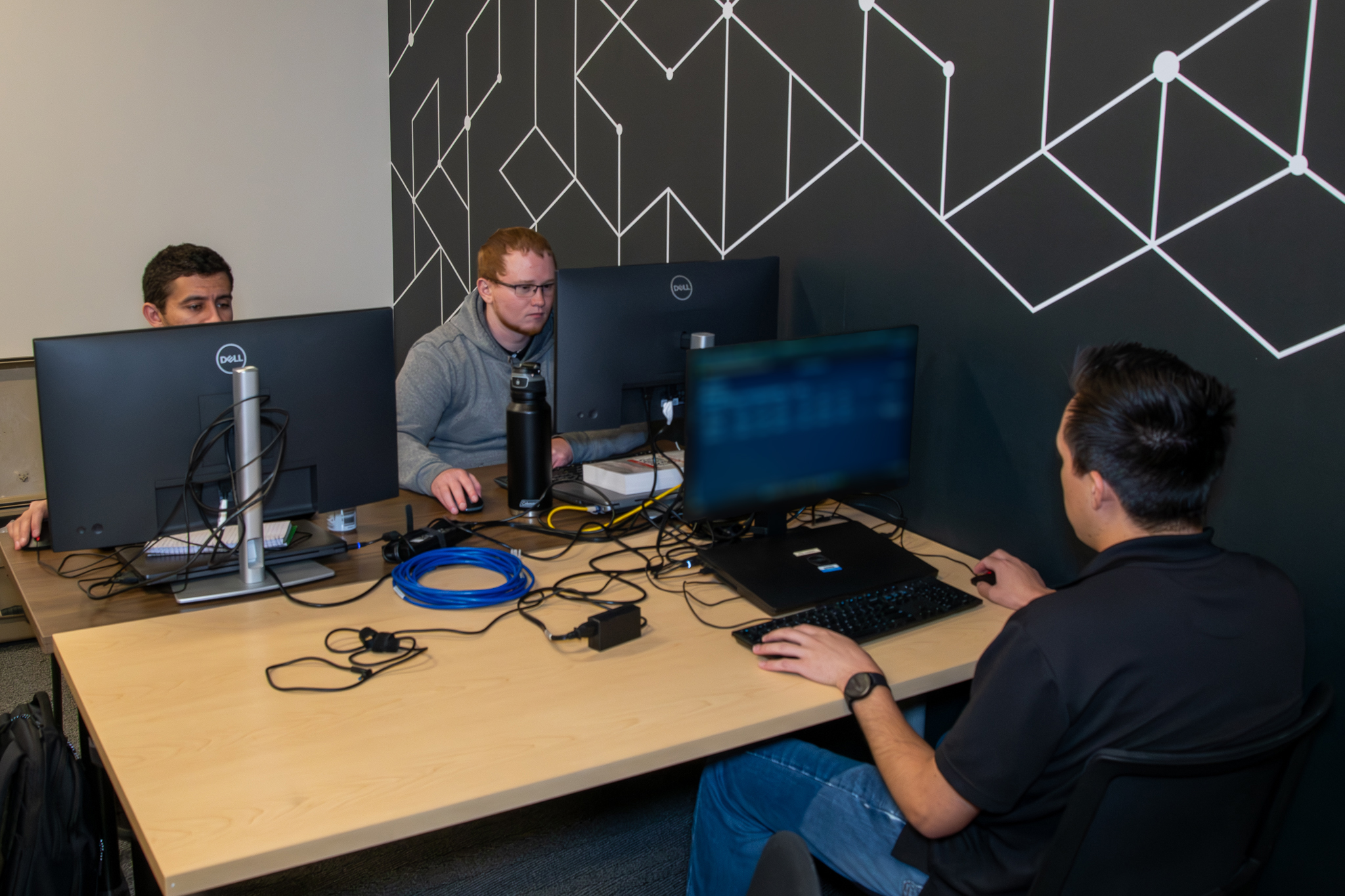 Three individuals are seated at a table working on desktop computers.