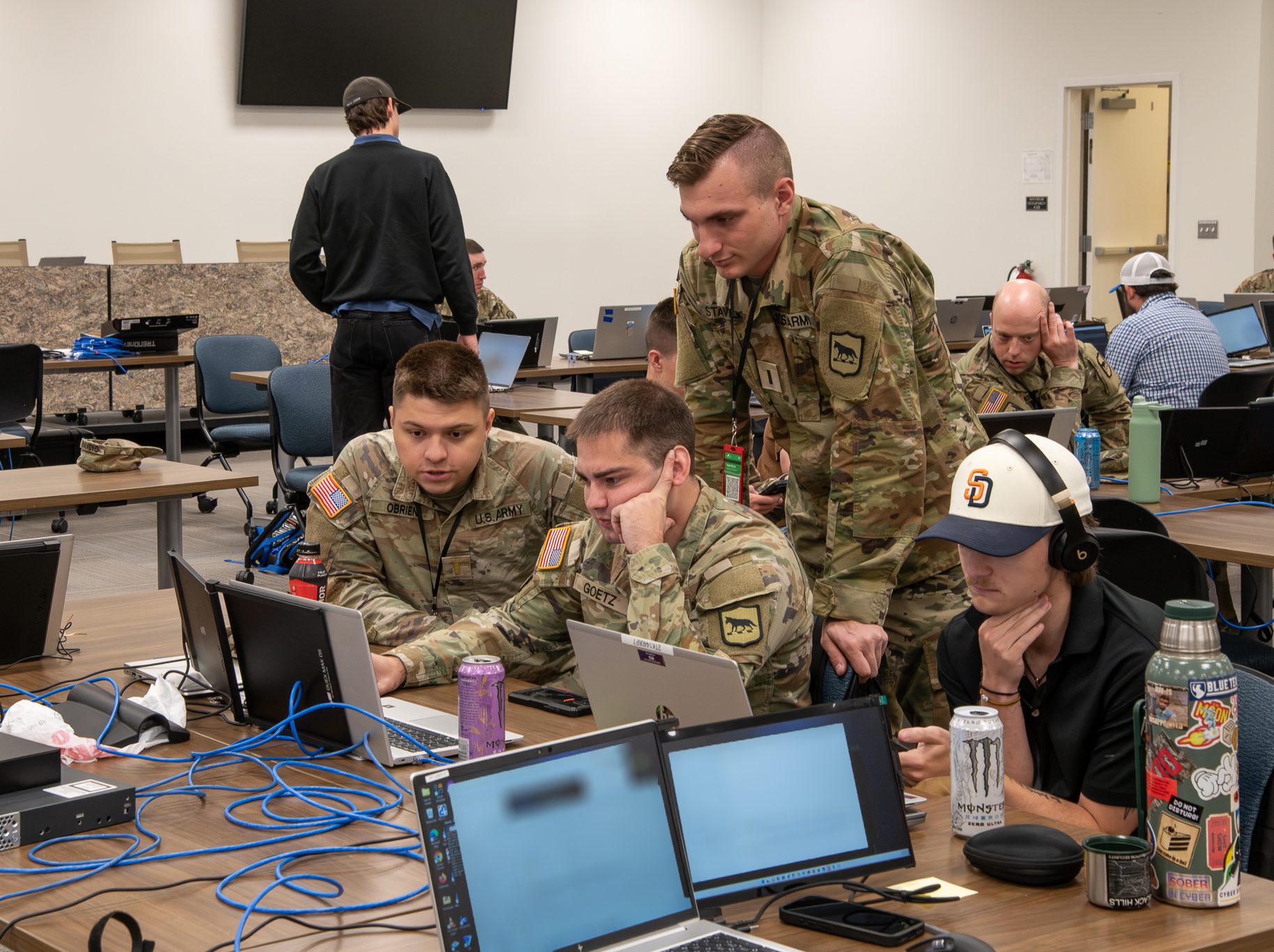 Individuals in uniform and others in casual clothing working together on laptops in a tech setup.