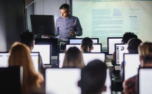 Male teacher giving a lecture from desktop PC during a class at computer lab.